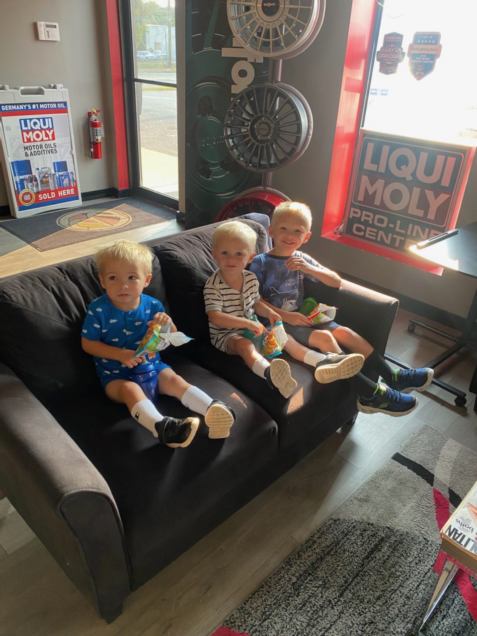 Three young boys sitting on a dark couch, holding snacks