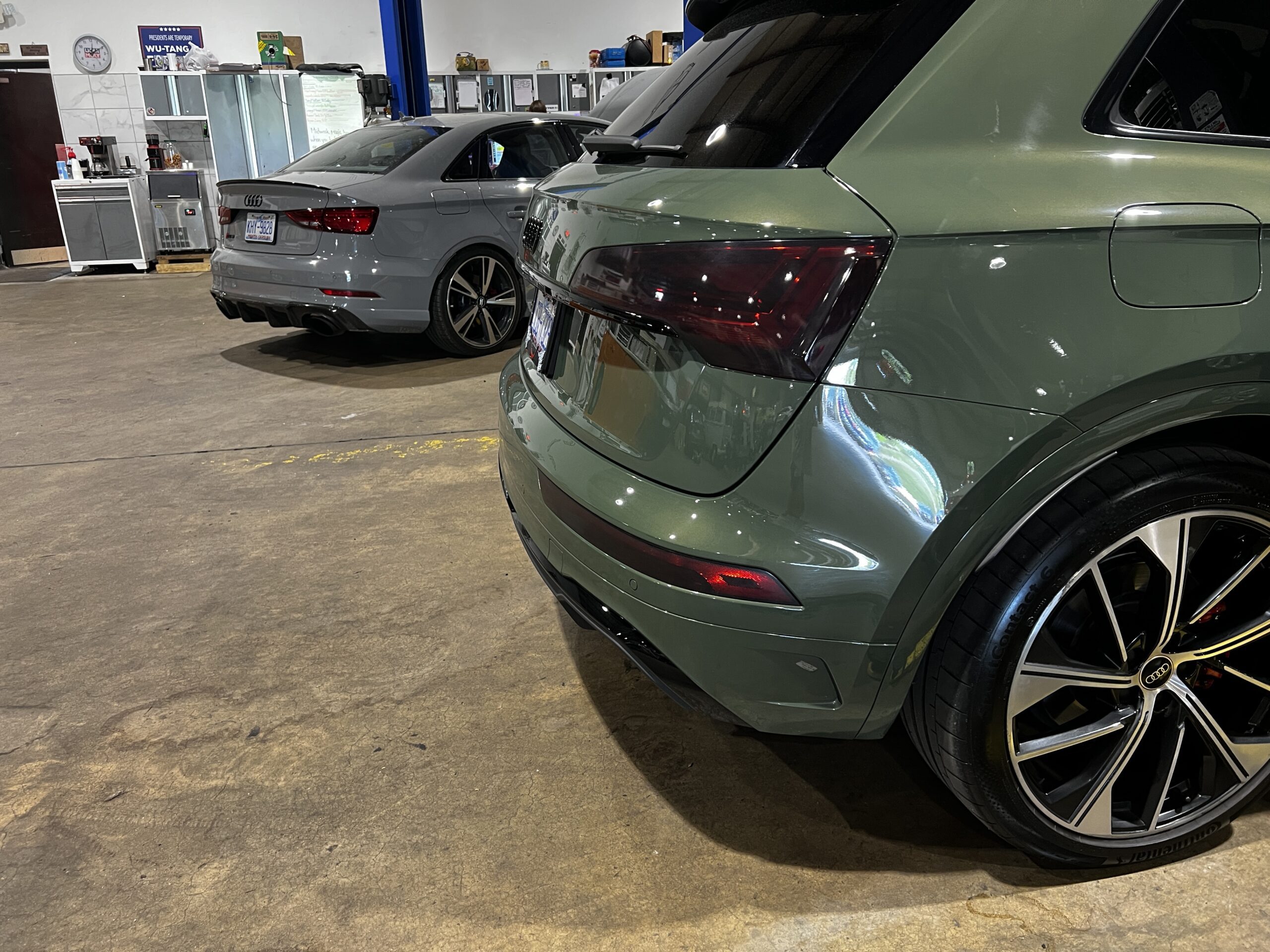 Two Audi cars, a grey sedan and a green SUV, at a Euro repair shop