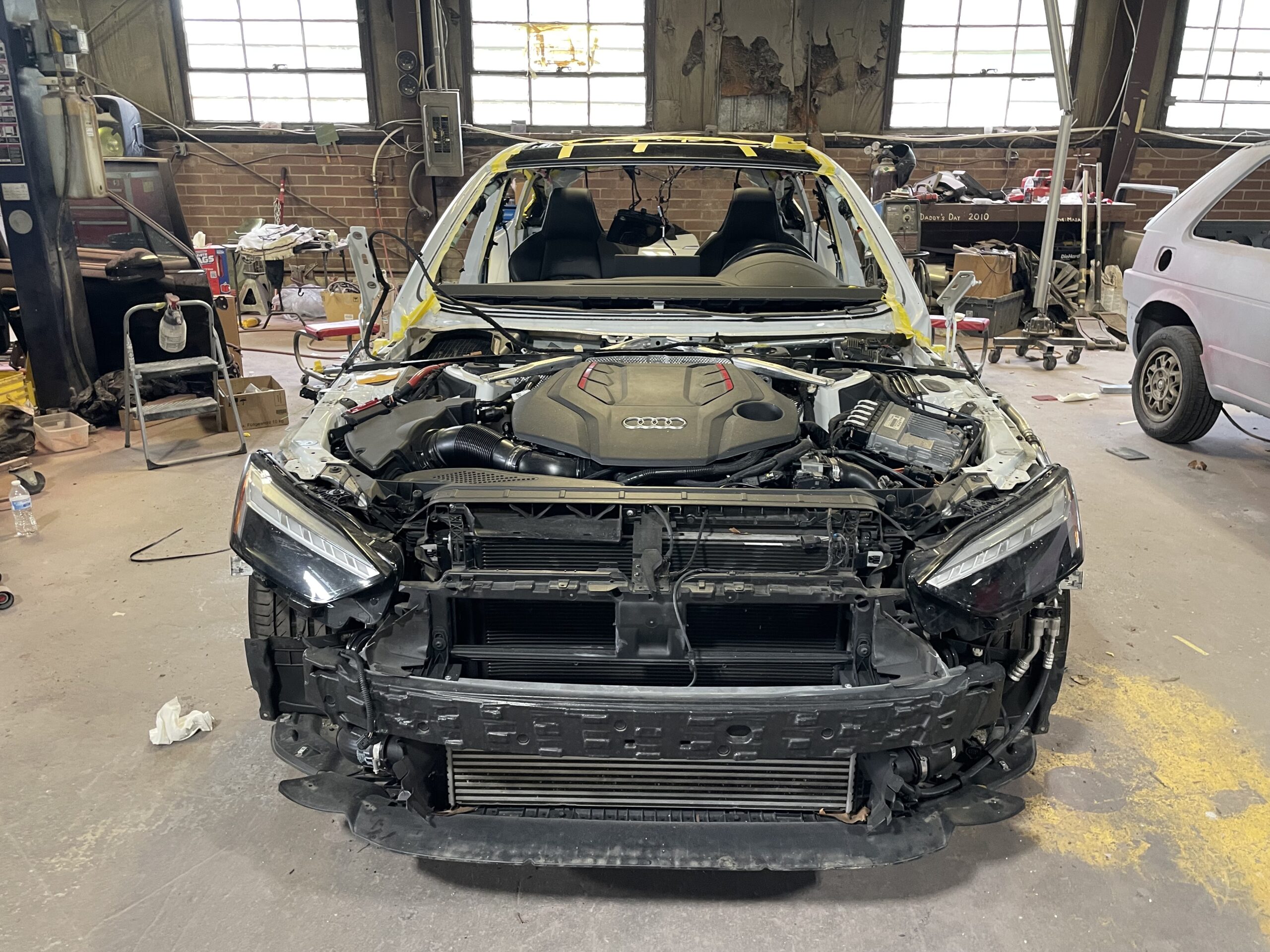 Audi RS5 front end disassembled in a Euro repair shop bay.