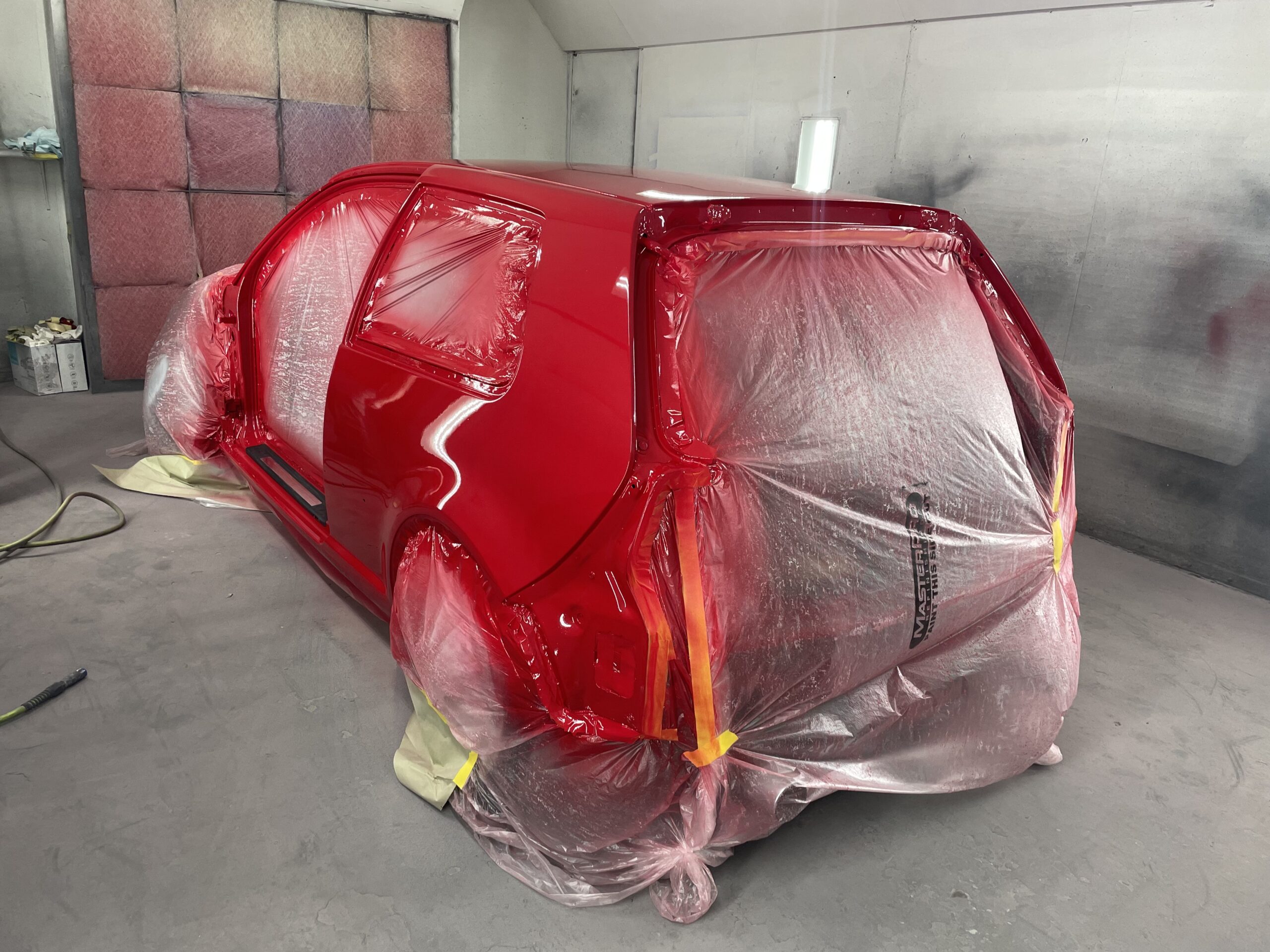 Red European car body in paint booth, ready for auto body repair