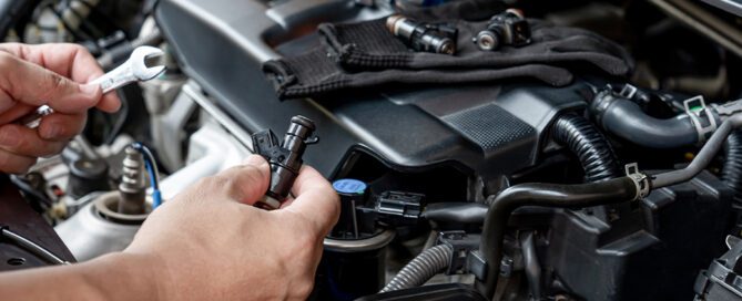 Mechanic holding fuel injector near car engine during service.