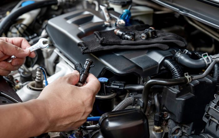 Mechanic holding fuel injector near car engine during service.